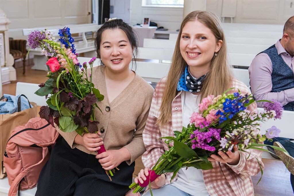 Twee jonge vrouwen die naast elkaar zitten en een bos bloemen vasthouden.